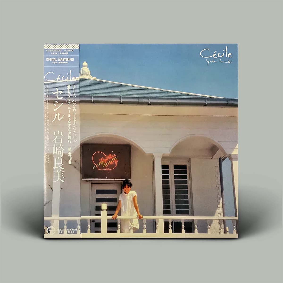 Cecile cover with a vertical spine, featuring a photograph of a woman in a white dress standing on a balcony in front of a building with arches under a blue sky.